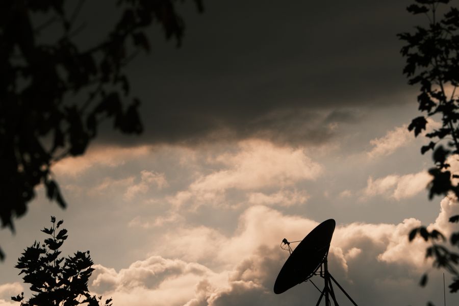 A satellite dish silhouetted against a stormy twilight sky